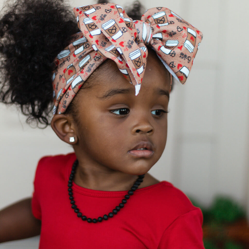 African American Baby Girl with Bow, Red Dress and Black Unpolished Baltic Amber Teething Necklace from Amber Guru, Posing Outside