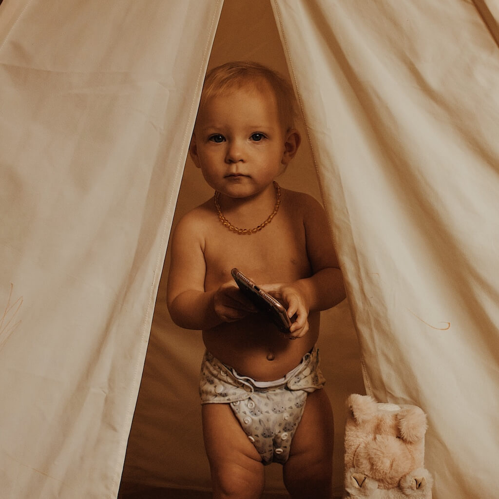 Baby Girl Holding the Phone and Wearing Premium Amber Teething Necklace for Children in Honey Color with Polished Beads