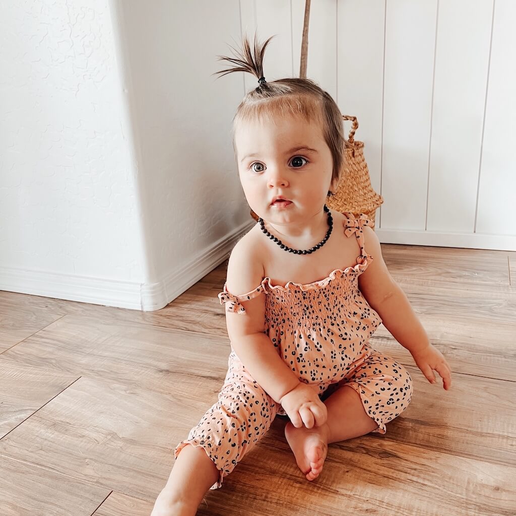 Baby Girl Wearing Amber Guru Amber Teething Necklace in Black Color with Raw/Unpolished Beads, Sitting in the Room