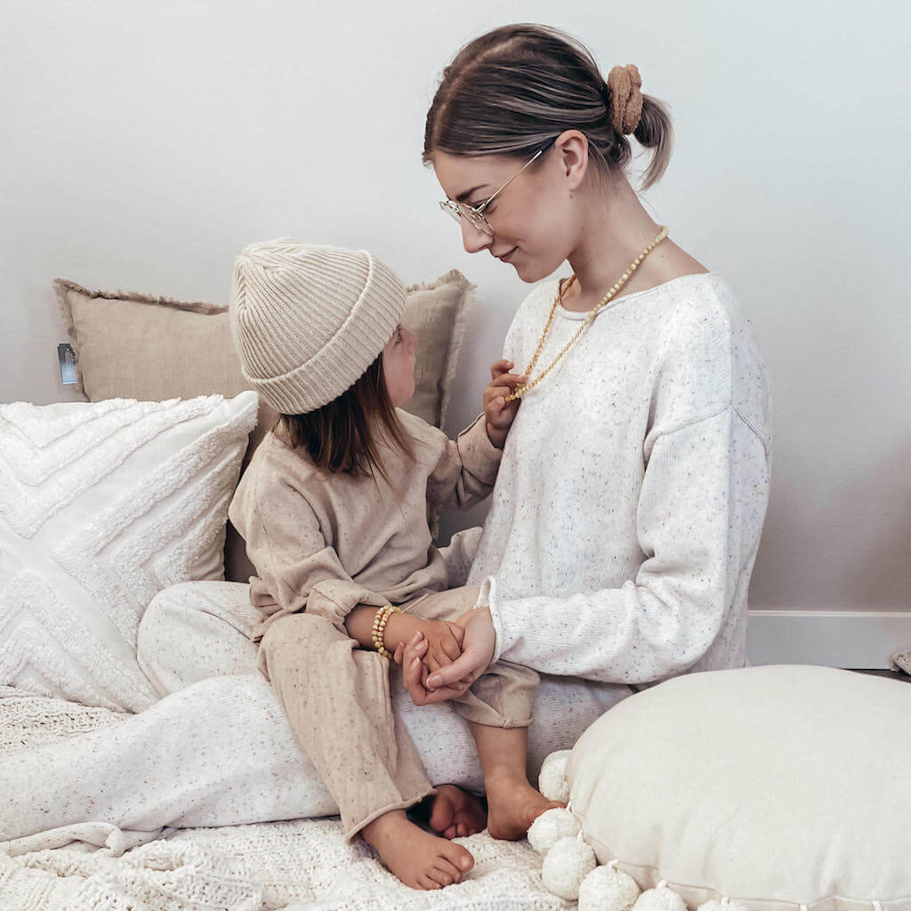 Boy with Long Hair Wearing Yellow Baltic Amber Teething Bracelet and His Mom Wearing Yellow Baltic Amber Necklace, Both Sitting on the Bed in the Room, for Amber Guru Photo Session