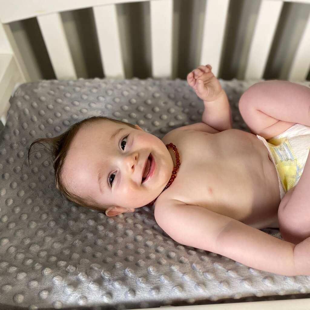 Happy Baby Boy Wearing Baltic Amber Teething Necklace in Cognac Color with Polished Beads from Amber Guru