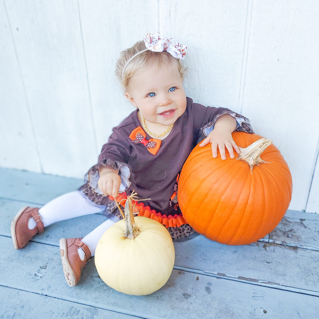 Little Girl Sitting with Pumpkin, Wearing Polished Baltic Amber Teething Necklace from Amber Guru in Butterscotch Color