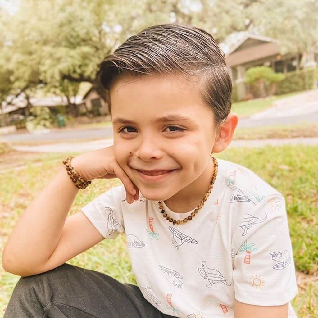 Smiling Kid Wearing Premium Rare Green Baltic Amber Necklace and Bracelet from Amber Guru, Sitting on the Grass Outside