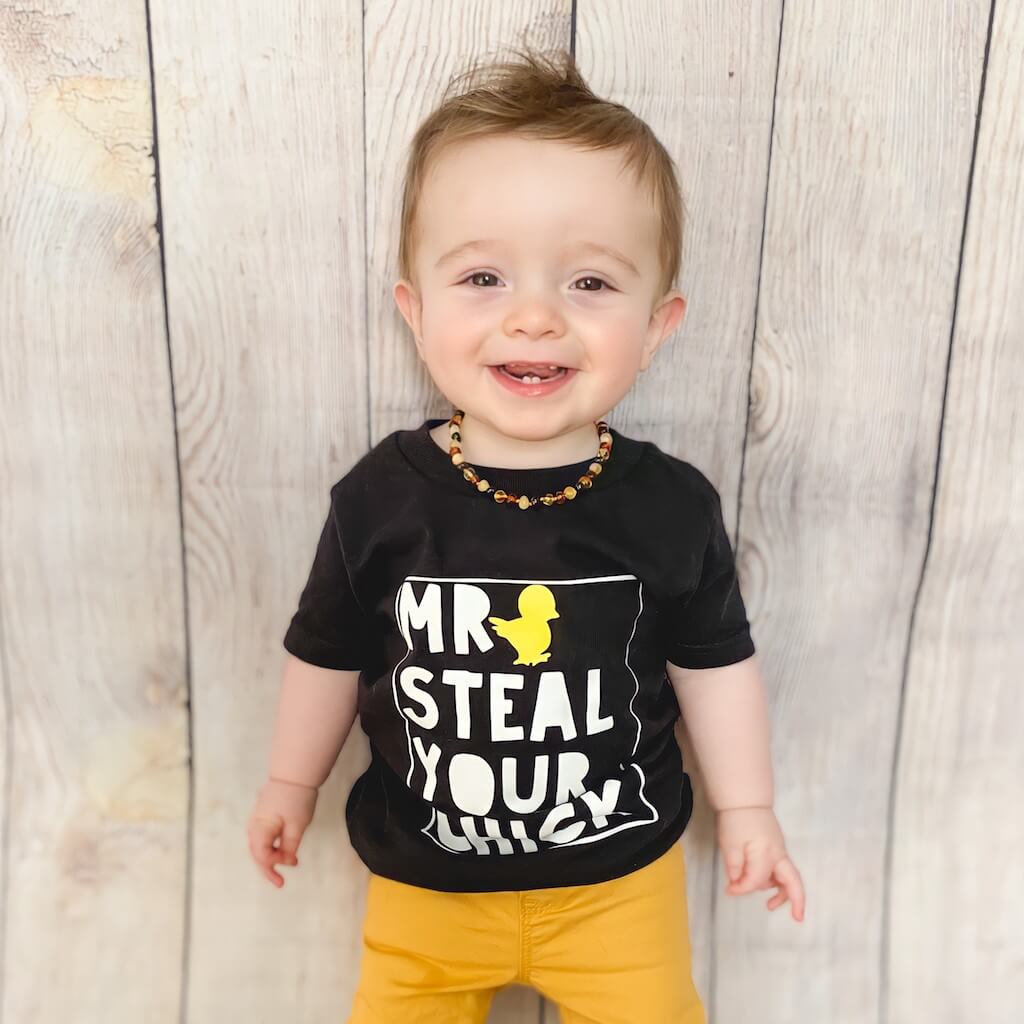 Teething Baby Boy Wearing Multi Colored Amber Guru Baltic Amber Necklace with Polished Beads, Standing by the Wall