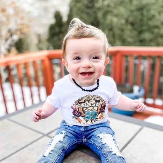 Teething Baby Boy, Wearing White T-shirt, Jeans and Raw Black Baltic Amber Necklace from Amber Guru, Sitting Outside