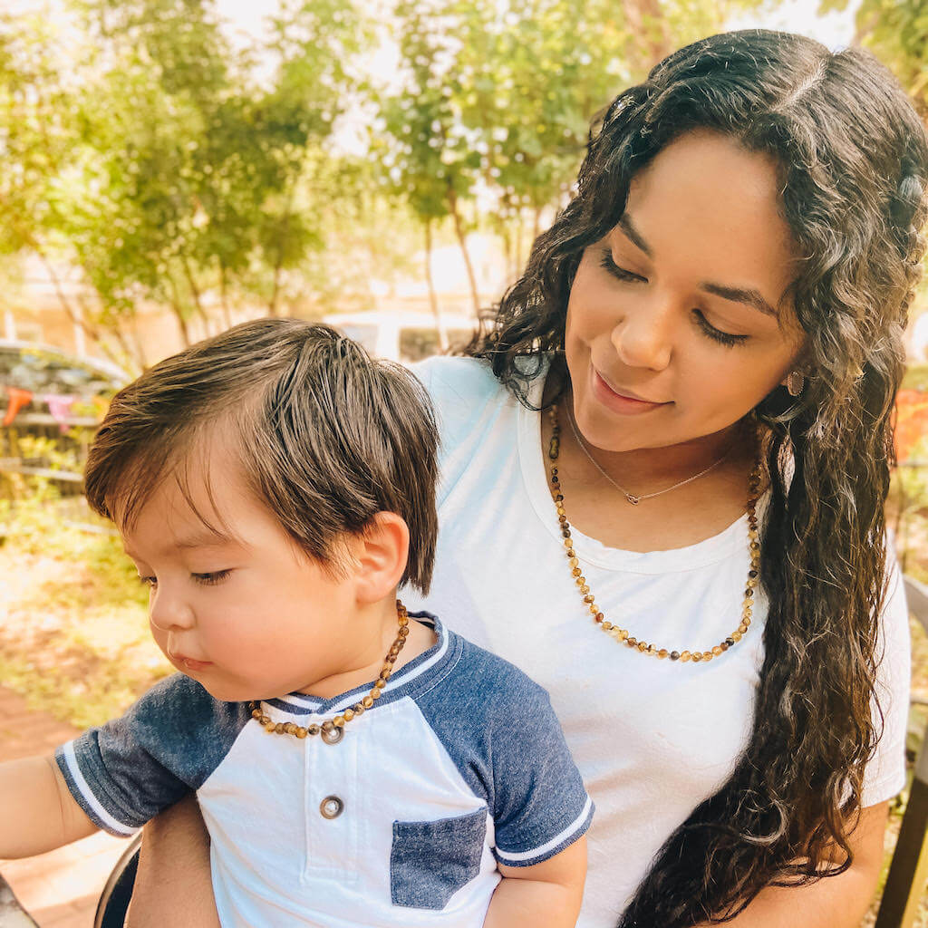 Teething Baby Boy and His Mother Wearing Premium Baltic Amber Necklaces in Green Color with Raw/Unpolished Beads from Amber Guru, Sitting in The Park