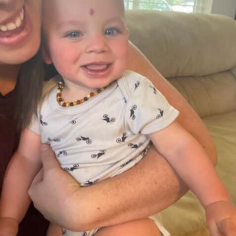 Smiling Baby Boy Wearing Amber Guru Premium Multicolor Baltic Amber Teething Necklace, Sitting on Mom's Knees