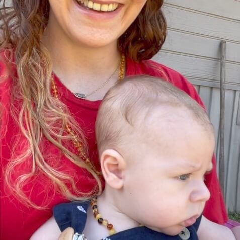 Smiling Mom Holding Her Baby Boy Who is Wearing Amber Guru Premium Baltic Amber Teething Necklace in Multi Color with Polished Beads to Help Relieve Teething Pain