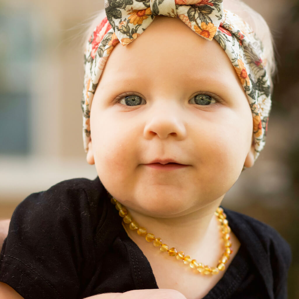 Baby Girl With Bow and Premium Baltic Amber Teething Necklace in Honey Color from Amber Guru