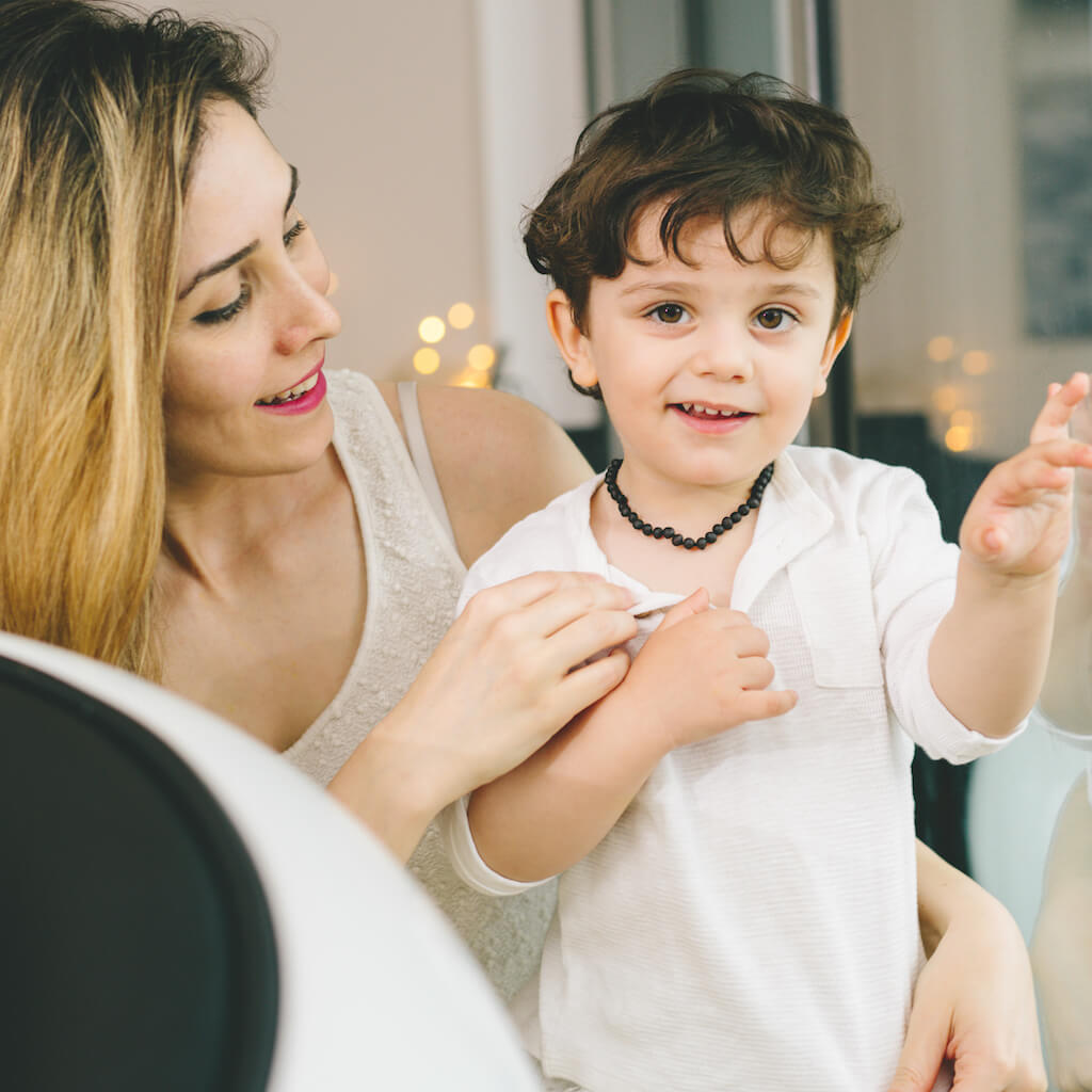 Happy Mom and Her Smiling Two Years Old Child with Black Unpolished Baltic Amber Teething Necklace from Amber Guru