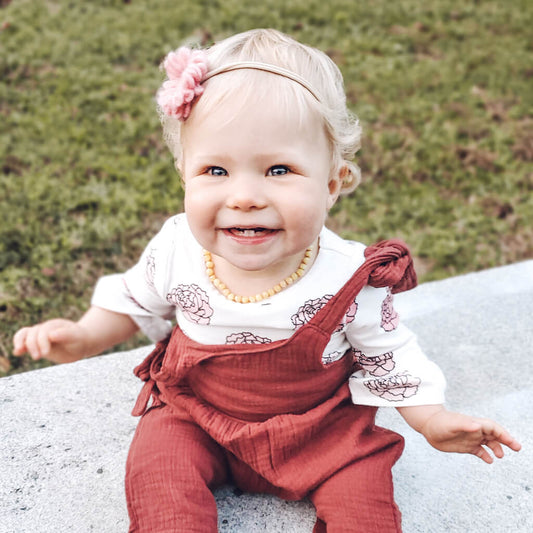 Happy Teething Baby Girl Wearing Yellow Baltic Amber Necklace from Amber Guru, Sitting Outside