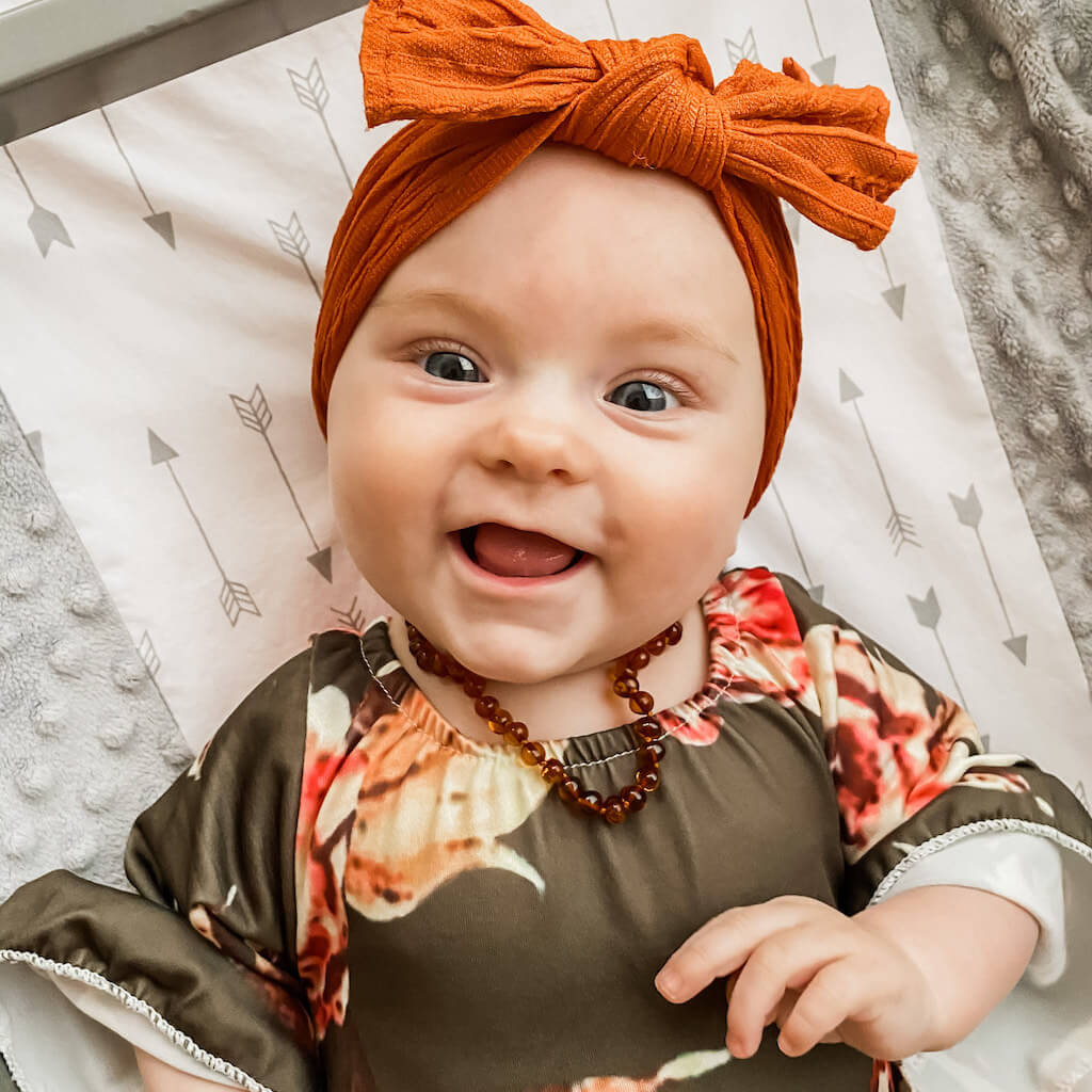 Smiling Baby Girl with Bow and Cognac Amber Teething Necklace from Amber Guru
